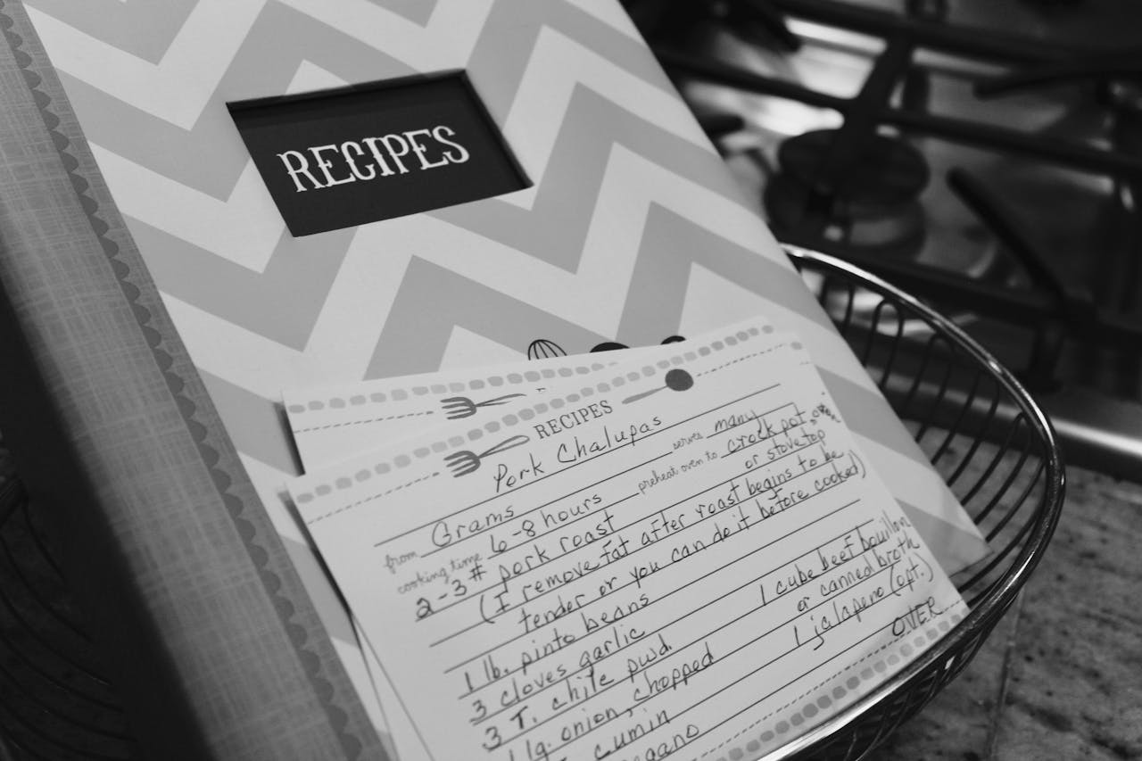 about-01 Monochrome image of a recipe book and handwritten notes in a kitchen setting.